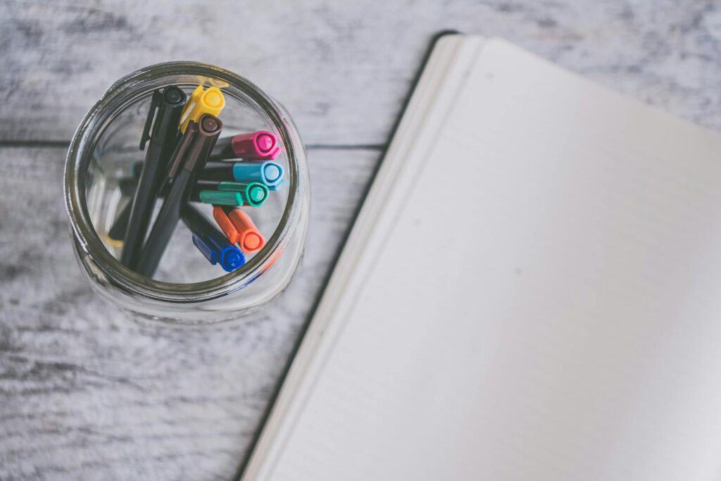 Clear Glass Jar Filled of Coloring Pens Beside a journal